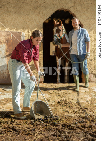 Young woman cleans manure near stable 140740164