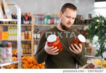 Man carefully selects canned tomatoes in the produce section of supermarket Man carefully selects canned tomatoes in the produce section of supermarket 140740267