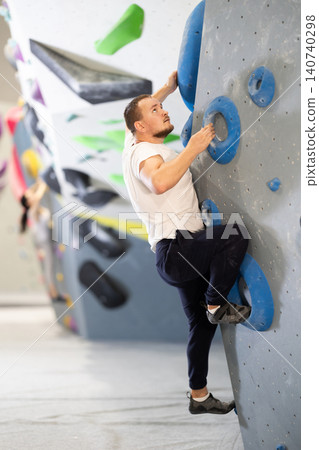 Man climbing a tall, indoor, man made rock climbing wall 140740298