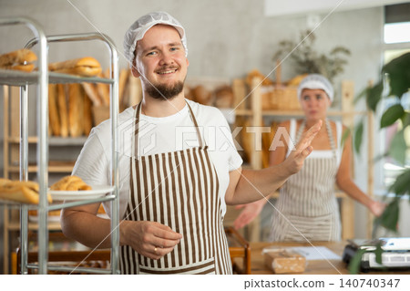 Content young man worker stands with his back to frustrated girl behind bakery counter Content young man worker stands with his back to frustrated girl behind bakery counter 140740347