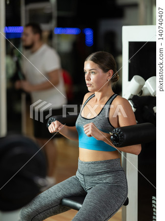 Girl in gym performs exercises for arm muscles using simulators and fitness center equipment. 140740407