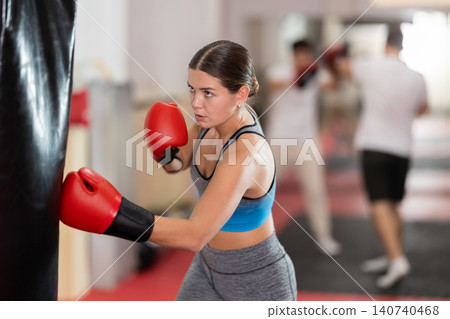 Girl punches and kicks punching bag in gym. Girl punches and kicks punching bag in gym. 140740468