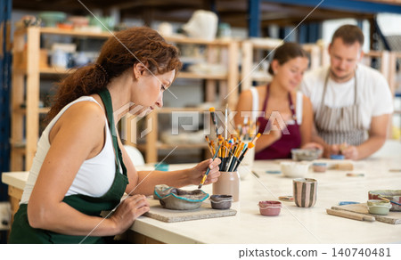 During workshop at master class, female employee paints clay vessel plate 140740481