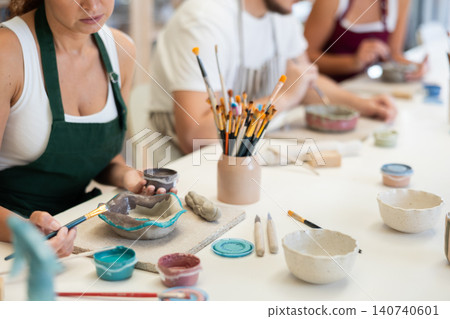 Three pottery masters work together on ceramic tableware, enjoying creative process as they paint mugs in workshop Three pottery masters work together on ceramic tableware, enjoying creative process as they paint mugs in workshop 140740601