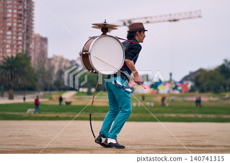 View of a bass drum with a cymbal, a man playing and spinning it, a Chilean chinchinero, a street musician playing the bass drum and dancing in the streets, a Chilean cultural tradition. View of a bass drum with a cymbal, a man playing and spinning it, a Chilean chinchinero, a street musician playing the bass drum and dancing in the streets, a Chilean cultural tradition. 140741315