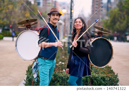 A couple of urban musicians and dancers, posing happily and romantically, with a bass drum on their backs outdoors, Chilean chinchineros, street musicians who play the bass drum and dance A couple of urban musicians and dancers, posing happily and romantically, with a bass drum on their backs outdoors, Chilean chinchineros, street musicians who play the bass drum and dance 140741322