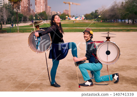 A couple of urban musicians, posing happily and romantically, she placing her foot on the man's knee, chinchineros, street musicians who play the bass drum and dance in the streets, Chilean cultural A couple of urban musicians, posing happily and romantically, she placing her foot on the man's knee, chinchineros, street musicians who play the bass drum and dance in the streets, Chilean cultural 140741339
