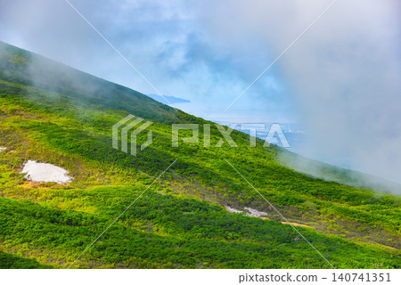 A clear summer day: Mount Chokai, with its green slopes and lingering snow, presents a mountainous landscape with white clouds rising nearby. 140741351