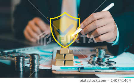 Businessman using stylus pen pointing at virtual shield checkmark icon on gold bars. Financial security, wealth protection, asset management and investment insurance concept. Businessman using stylus pen pointing at virtual shield checkmark icon on gold bars. Financial security, wealth protection, asset management and investment insurance concept. 140741404