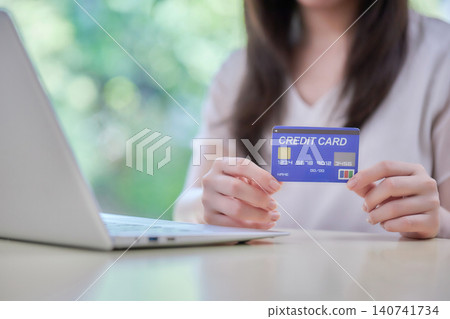 A woman in her 20s enters information into a computer while looking at her credit card. A woman in her 20s enters information into a computer while looking at her credit card. 140741734