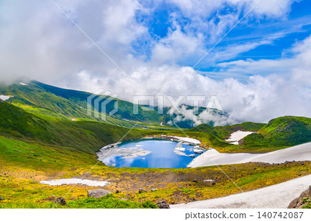 On a clear summer day, snowdrifts adorn the mystical crater lake, Lake Chokai, on Mount Chokai, creating a beautiful reflection of the summer sky. On a clear summer day, snowdrifts adorn the mystical crater lake, Lake Chokai, on Mount Chokai, creating a beautiful reflection of the summer sky. 140742087