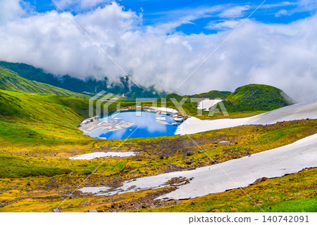 On a clear summer day, snowdrifts adorn the mystical crater lake, Lake Chokai, on Mount Chokai, creating a beautiful reflection of the summer sky. 140742091