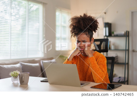 Young black woman in cozy sweater concentrating on laptop at home office during daytime. Young black woman in cozy sweater concentrating on laptop at home office during daytime. 140742465