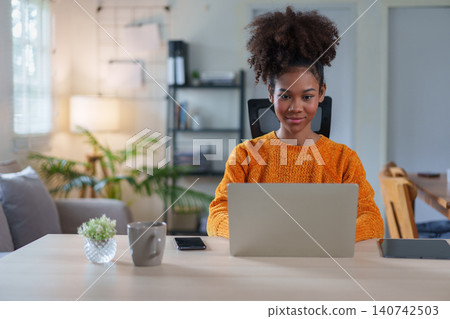Young African American woman smiling while engaged in virtual meeting at home. Young African American woman smiling while engaged in virtual meeting at home. 140742503