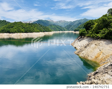 The snow-capped mountains reflected in the mirror-like surface of Yagisawa Dam Lake, and the lush green mountain scenery. The snow-capped mountains reflected in the mirror-like surface of Yagisawa Dam Lake, and the lush green mountain scenery. 140742731