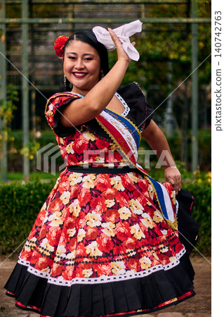 Portrait of a beautiful, smiling young woman, happily dressed in a Chilean huasa, celebrating, playing with her handkerchief, and posing to dance cueca, a traditional Chilean dance. Chilean traditions Portrait of a beautiful, smiling young woman, happily dressed in a Chilean huasa, celebrating, playing with her handkerchief, and posing to dance cueca, a traditional Chilean dance. Chilean traditions 140742763
