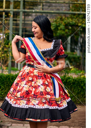 Portrait of a beautiful young woman smiling, cheerfully dressed as a Chilean huasa, joyfully celebrating and posing to dance the cueca, a traditional Chilean dance. Chilean traditions. Portrait of a beautiful young woman smiling, cheerfully dressed as a Chilean huasa, joyfully celebrating and posing to dance the cueca, a traditional Chilean dance. Chilean traditions. 140742789