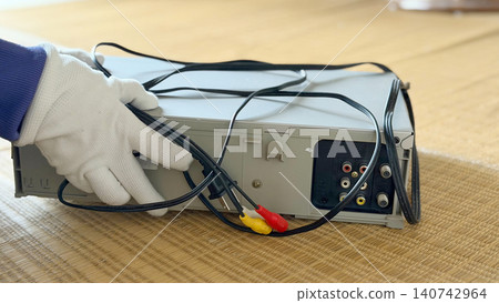 A hand wearing white gloves holding an old VCR - from the back left. A hand wearing white gloves holding an old VCR - from the back left. 140742964