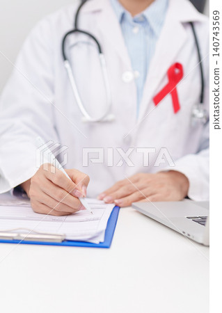 doctor using laptop and report notes on notebook. red ribbon concept of December World Aids Day, MADD, October Red ribbon week, February Heart month, Marfan Syndrome, May Stroke awareness doctor using laptop and report notes on notebook. red ribbon concept of December World Aids Day, MADD, October Red ribbon week, February Heart month, Marfan Syndrome, May Stroke awareness 140743569