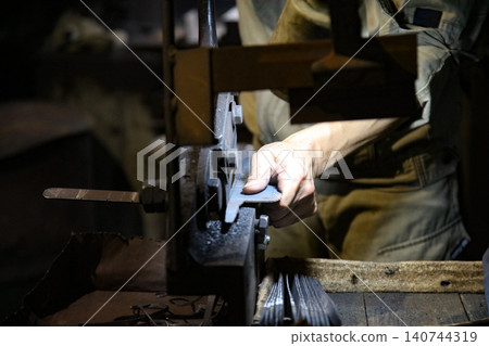 A craftsman uses a hand shear to cut the material into the shape of a knife A craftsman uses a hand shear to cut the material into the shape of a knife 140744319