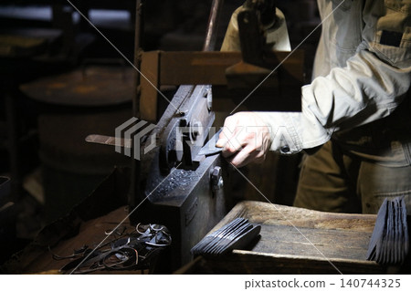 A craftsman uses a hand shear to cut the material into the shape of a knife A craftsman uses a hand shear to cut the material into the shape of a knife 140744325