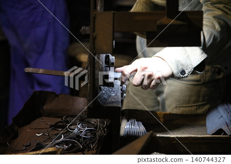 A craftsman uses a hand shear to cut the material into the shape of a knife 140744327