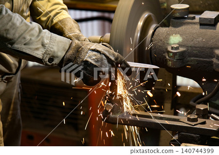 A craftsman shaping the metal using a grinder 140744399