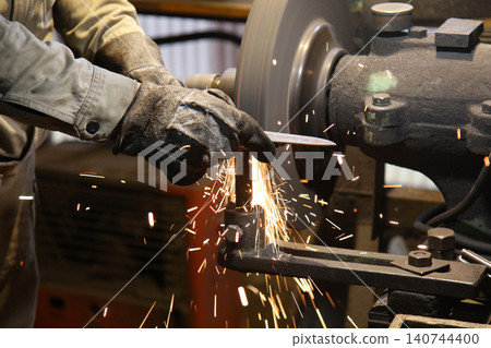 A craftsman shaping the metal using a grinder A craftsman shaping the metal using a grinder 140744400
