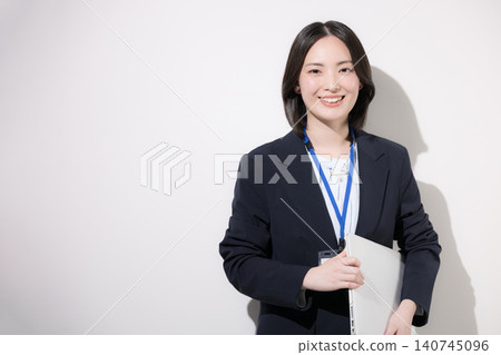 一位面帶微笑的年輕女上班族，在白色背景前使用筆記型電腦；照片中她正在辦公室工作，直視鏡頭。 140745096