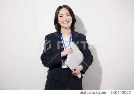 A smiling young female office worker with a laptop against a white background; an image of her working in an office, looking directly at the camera. 140745097