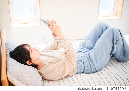 一位二十多歲的日本女性在床上放鬆地玩遊戲。 一位二十多歲的日本女性在床上放鬆地玩遊戲。 140745594