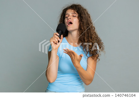 Woman enthusiastically singing into microphone expressive joyful performance musical vocal talent Woman enthusiastically singing into microphone expressive joyful performance musical vocal talent 140746104