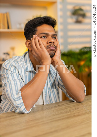 Indian man on home table leaning on hands looking exhausted after long remote work indoors at home Indian man on home table leaning on hands looking exhausted after long remote work indoors at home 140746124