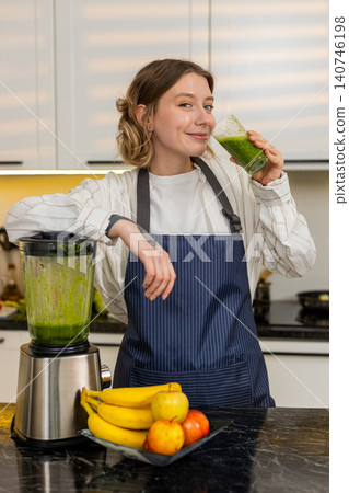 Young woman pouring green smoothie into glass in home kitchen for healthy diet meal and clean eating Young woman pouring green smoothie into glass in home kitchen for healthy diet meal and clean eating 140746198
