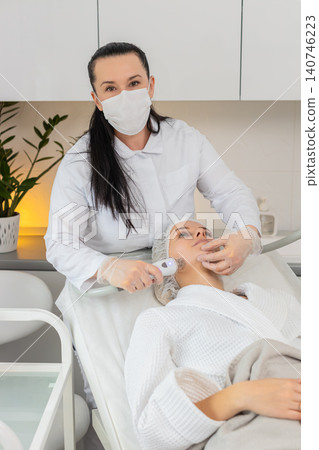 Woman receives RF lifting facial massage therapy by cosmetologist using professional equipment Woman receives RF lifting facial massage therapy by cosmetologist using professional equipment 140746223