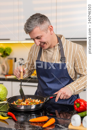 Middle-aged man tasting fried vegetables in kitchen during diet meal preparation and healthy eating 140746303