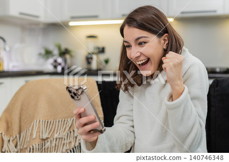 Young woman celebrates finance app balance rise on smartphone makes victory fist, win victory game Young woman celebrates finance app balance rise on smartphone makes victory fist, win victory game 140746348
