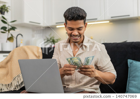 Indian man checks dollar cash with laptop spreadsheet enters sums confirm goal smiles bonus invest Indian man checks dollar cash with laptop spreadsheet enters sums confirm goal smiles bonus invest 140747069
