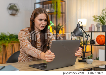Young woman waves hand in frustration as laptop freezes with virus glitch error then exhales to calm 140747074