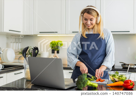 Young woman slicing cucumber for keto salad while watching recipe video on laptop pc in home kitchen Young woman slicing cucumber for keto salad while watching recipe video on laptop pc in home kitchen 140747086