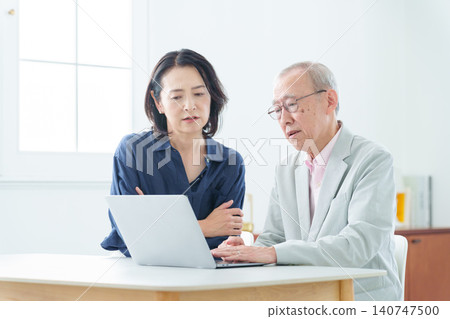 An elderly man using a computer with a troubled expression. 140747500