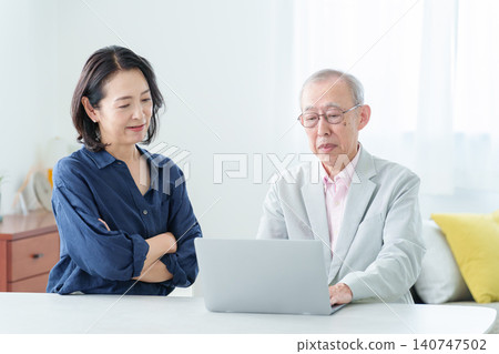 An elderly man using a computer with a troubled expression. 140747502