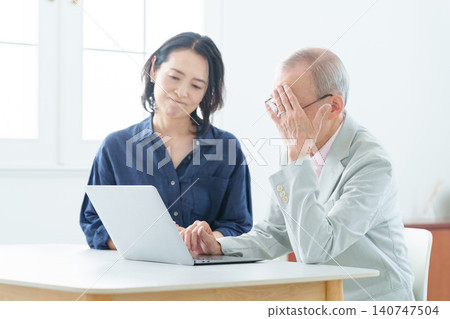 An elderly man using a computer with a troubled expression. 140747504