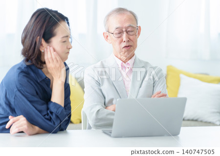 An elderly man using a computer with a troubled expression. 140747505