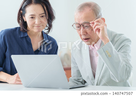 An elderly man using a computer with a troubled expression. 140747507