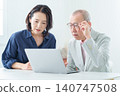 An elderly man using a computer with a troubled expression. 140747508