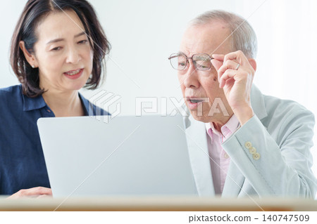 An elderly man using a computer with a troubled expression. 140747509