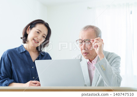 An elderly man using a computer with a troubled expression. 140747510