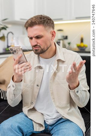 Young man gets alarming smartphone alert frowns asks why it happened anxious reaction worried mood 140747646