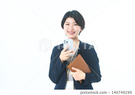 A woman holding a smartphone and a notebook smiles and looks directly at the camera. A woman holding a smartphone and a notebook smiles and looks directly at the camera. 140749299